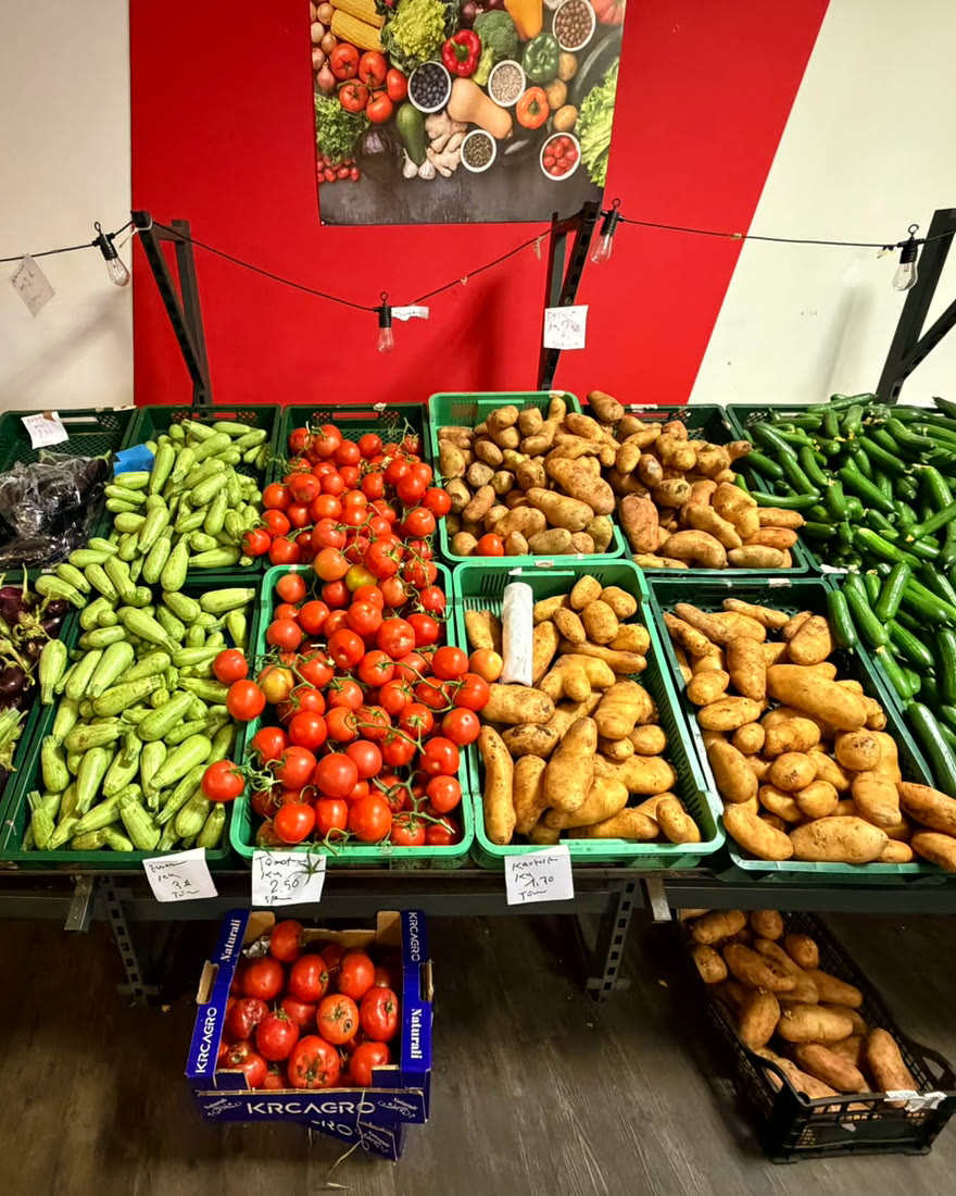 Tomaten, Zucchini, Kartoffeln und Gurken in grünen Kisten vor der roten Wand